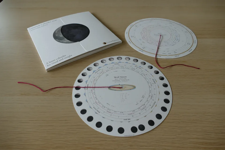 Folded Lunation Calendar prototype beside a year chart and a Wolf Moon chart crossed by a burgundy thread marker.
